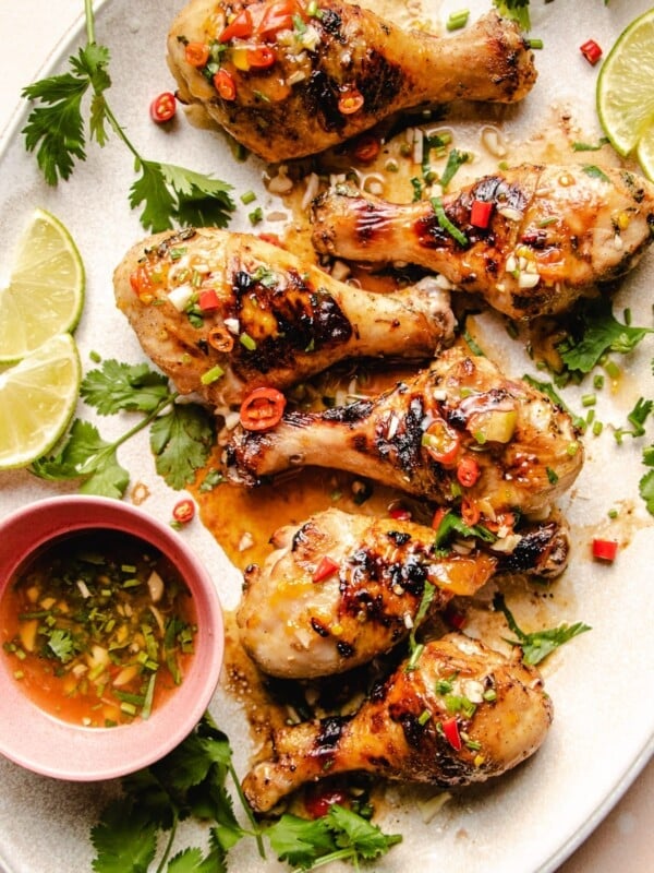 Photo shows 6 grilled chicken legs drizzled with sauce on a big white oval plate