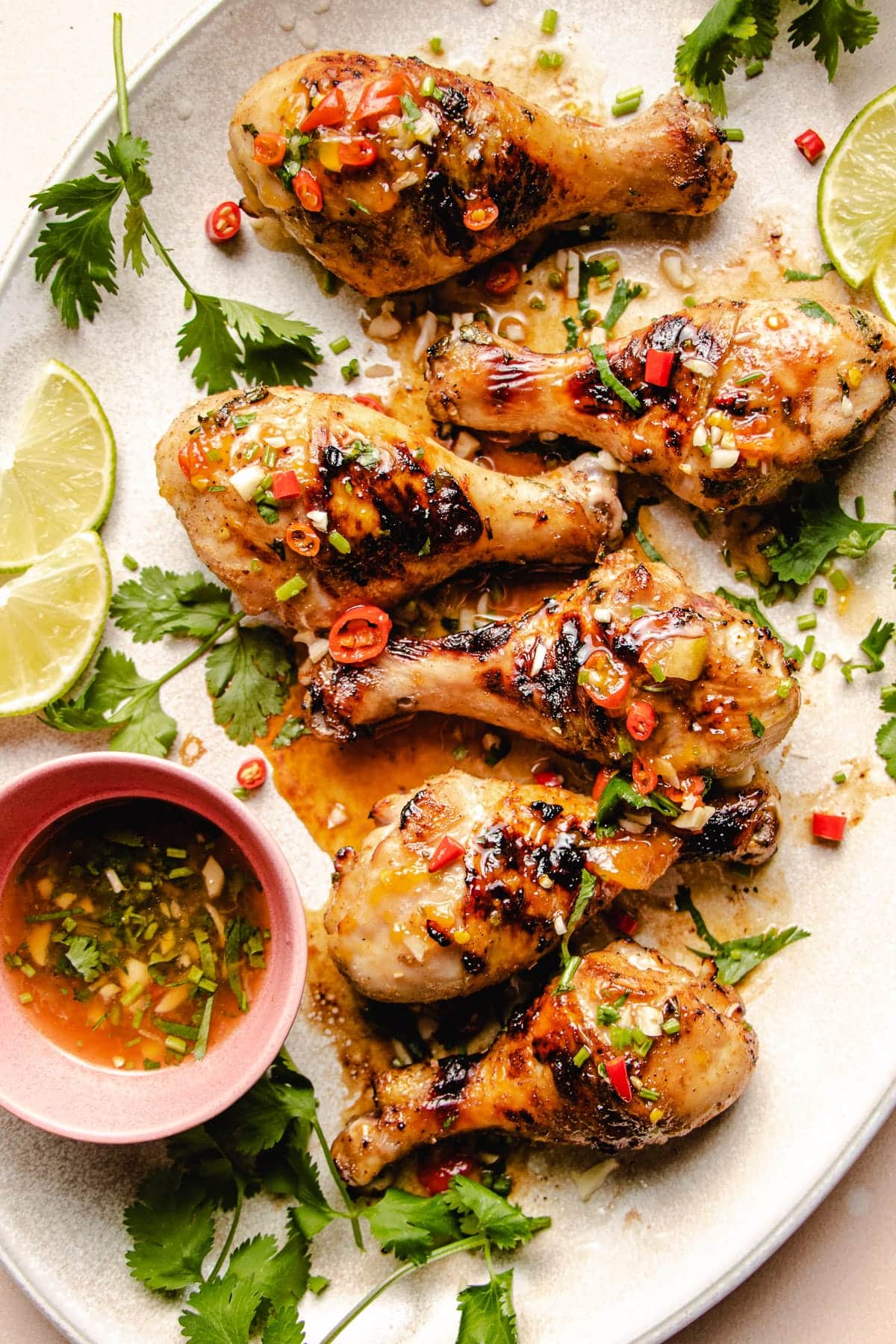 Photo shows 6 grilled chicken legs drizzled with sauce on a big white oval plate