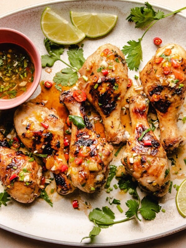 Photo shows bbq Vietnamese grilled chicken drumsticks with dipping sauce on the side and extra lime served on a big white oval plate