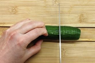 Photo shows straight cutting a cucumber with two chopsticks on the side and holding knife at a straight angle