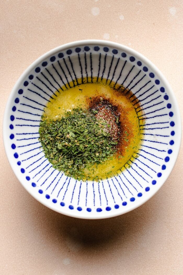 Photo shows a small white blue color bowl with butter herb seasoning sauce