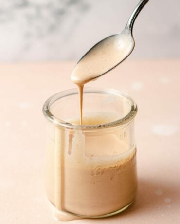 Creamy tangy sauce in a glass jar with a spoonful of sauce dripping out