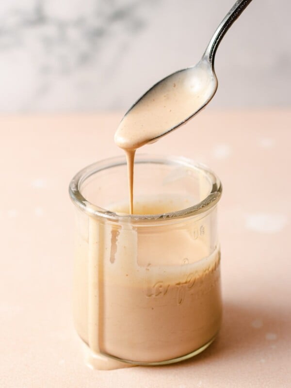 Creamy tangy sauce in a glass jar with a spoonful of sauce dripping out