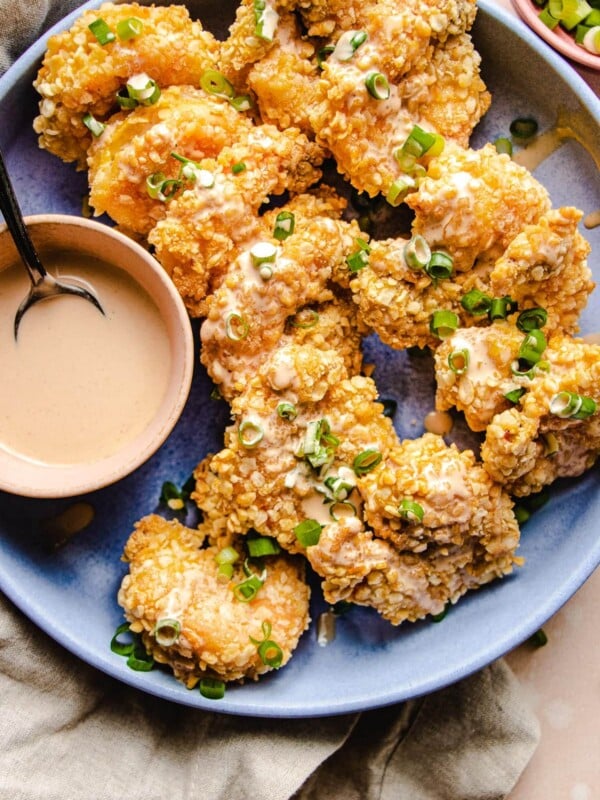 A plate of jumbo air fried bang bang shrimp served over a big blue/purple color plate with the sauce on the side