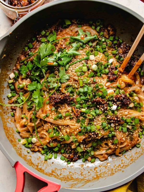 rice noodles tossed with garlic chili sauce oil in a saute pan with chopsticks on the side.