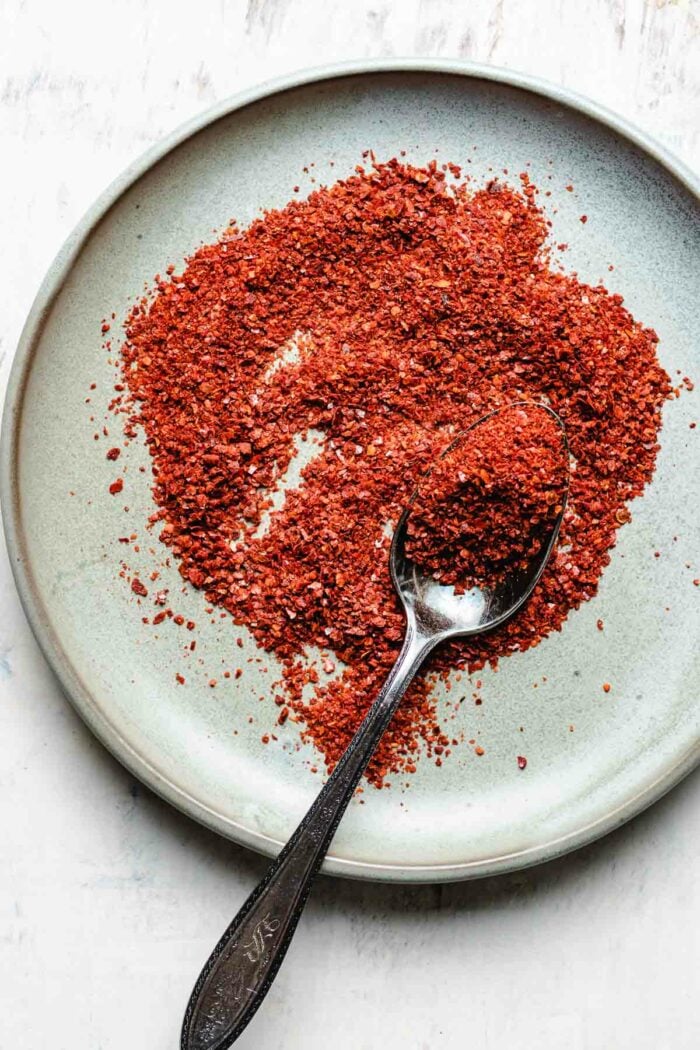 A plate of Korean red pepper flakes gochugaru displayed on a small plate with a spoon on the side