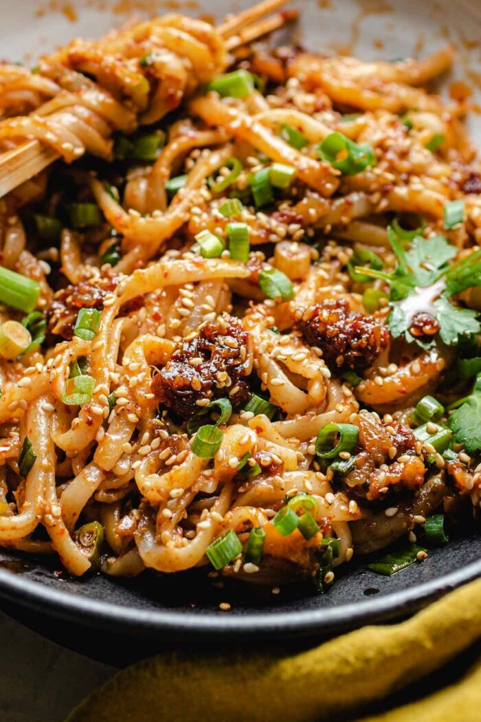 A close shot shows noodles tossed with garlic chili sauce and served on a plate
