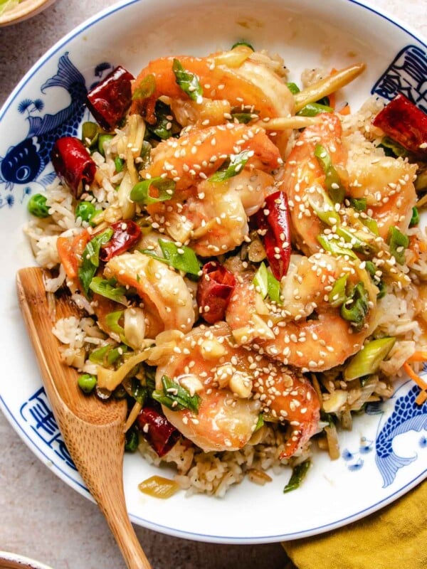 Large shrimp coated with general tso sauce served with rice in a blue white color plate.