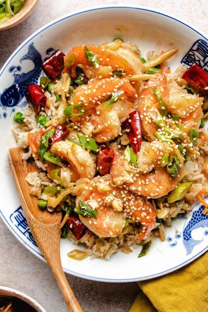 Large shrimp coated with general tso sauce served with rice in a blue white color plate.