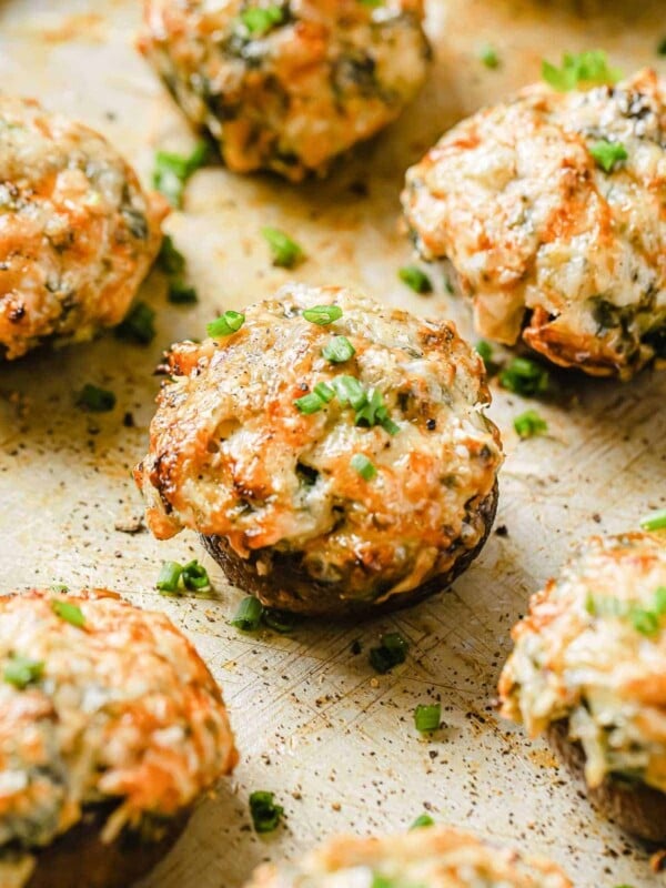 A close shot shows several cheese and creamy cheese spinach stuffed keto mushrooms baked over a lined sheet pan