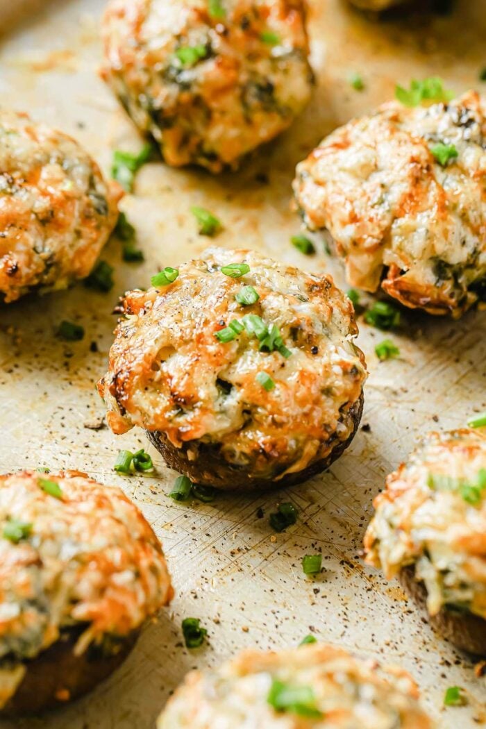 A close shot shows several cheese and creamy cheese spinach stuffed keto mushrooms baked over a lined sheet pan