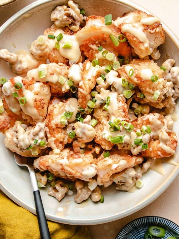 A close shot shows golden brown fried shrimp with walnuts drizzled with honey sauce served in a big white plate