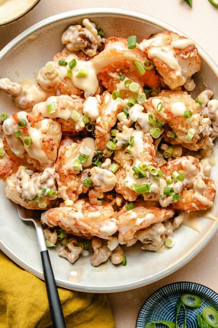 A close shot shows golden brown fried shrimp with walnuts drizzled with honey sauce served in a big white plate