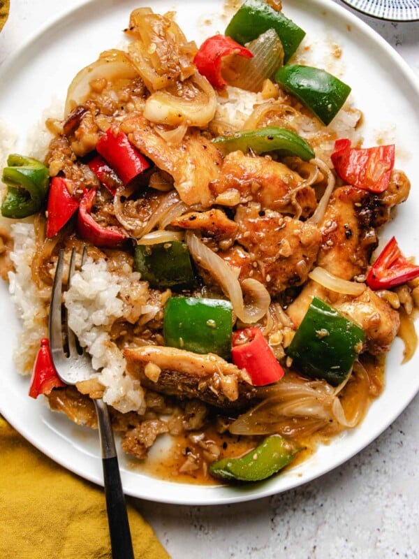 Sha cha chicken served with white rice on a white color plate with yellow napkin on the side and a fork