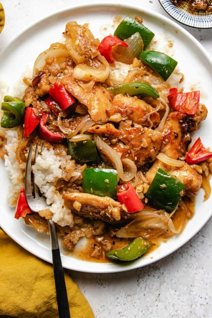 Sha cha chicken served with white rice on a white color plate with yellow napkin on the side and a fork