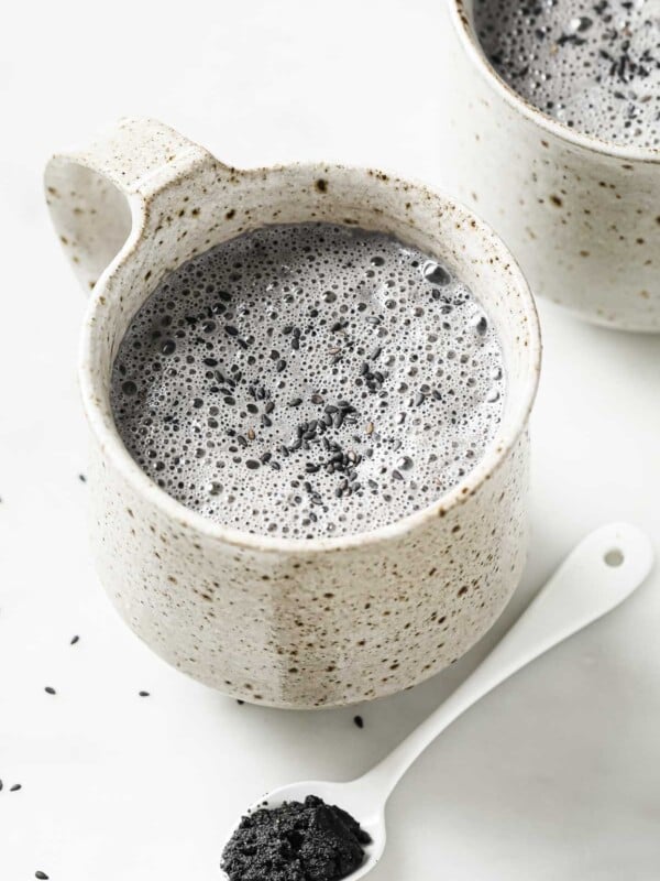 2 white color mugs with black sesame latte milk drink and a small teaspoon of black sesame paste on the side