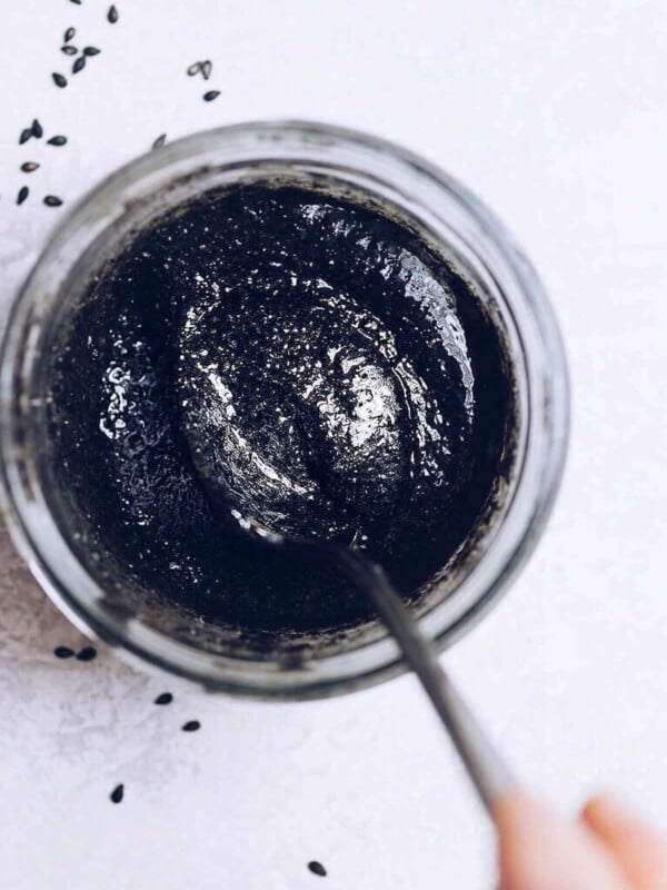 Photo shows a thick black sesame paste in a glass jar with a spoon stirring