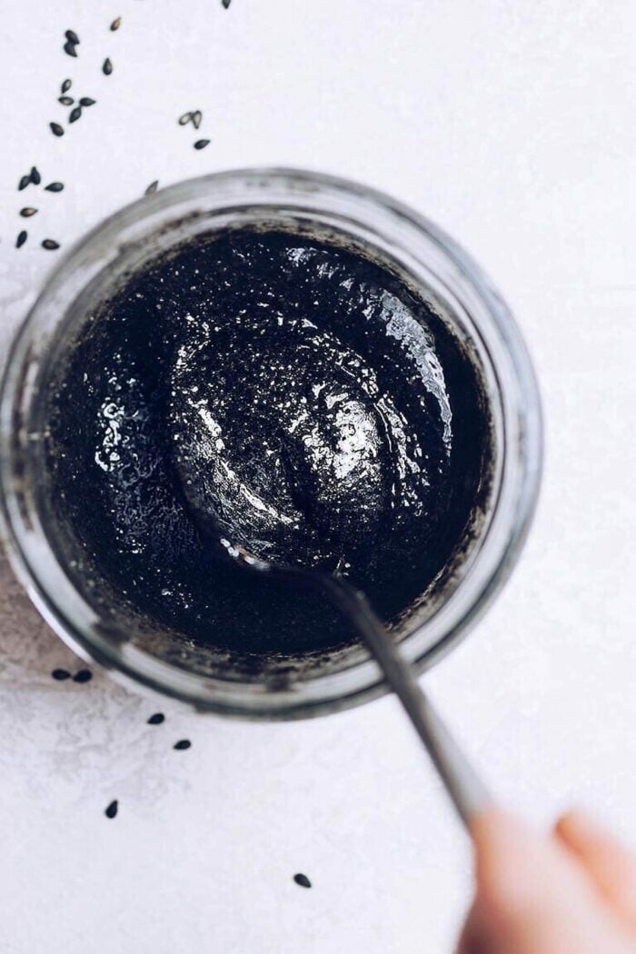 Photo shows a thick black sesame paste in a glass jar with a spoon stirring