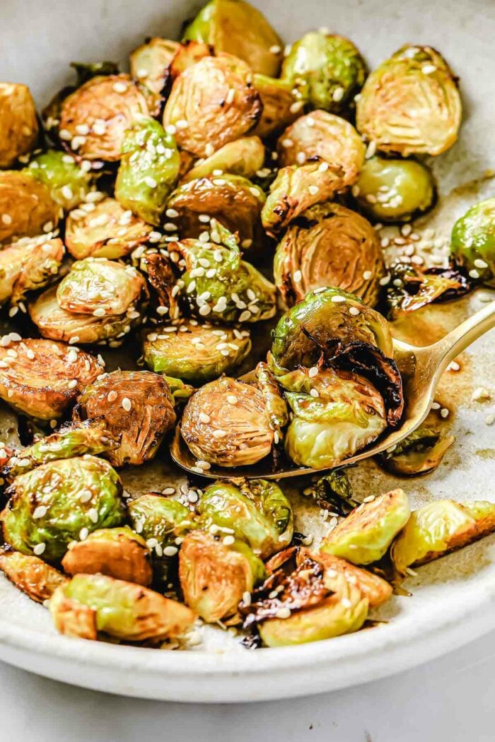 A side close shot shows crispy texture of the Asian brussels sprouts served over a big white plate