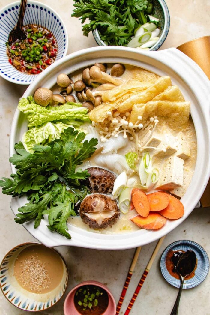 Photo shows a hot pot loaded with vegetables with dipping sauces on the side