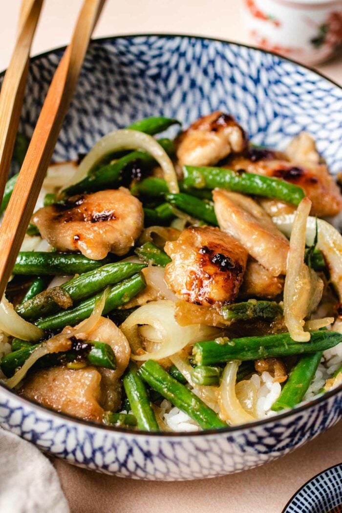 a side close shot shows string bean chicken served in a light blue color bowl with rice