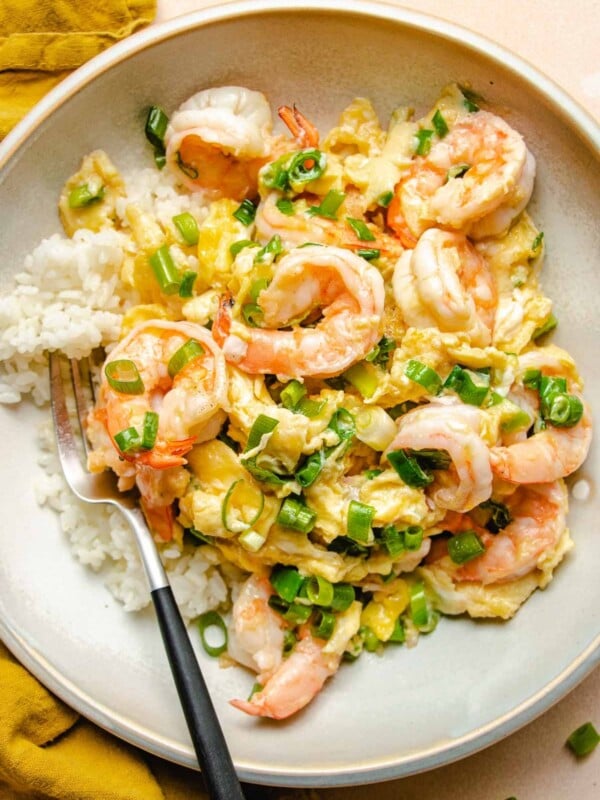 A close shot shows silky scrambled eggs with shrimp served over a bed of steamed white rice on a white plate