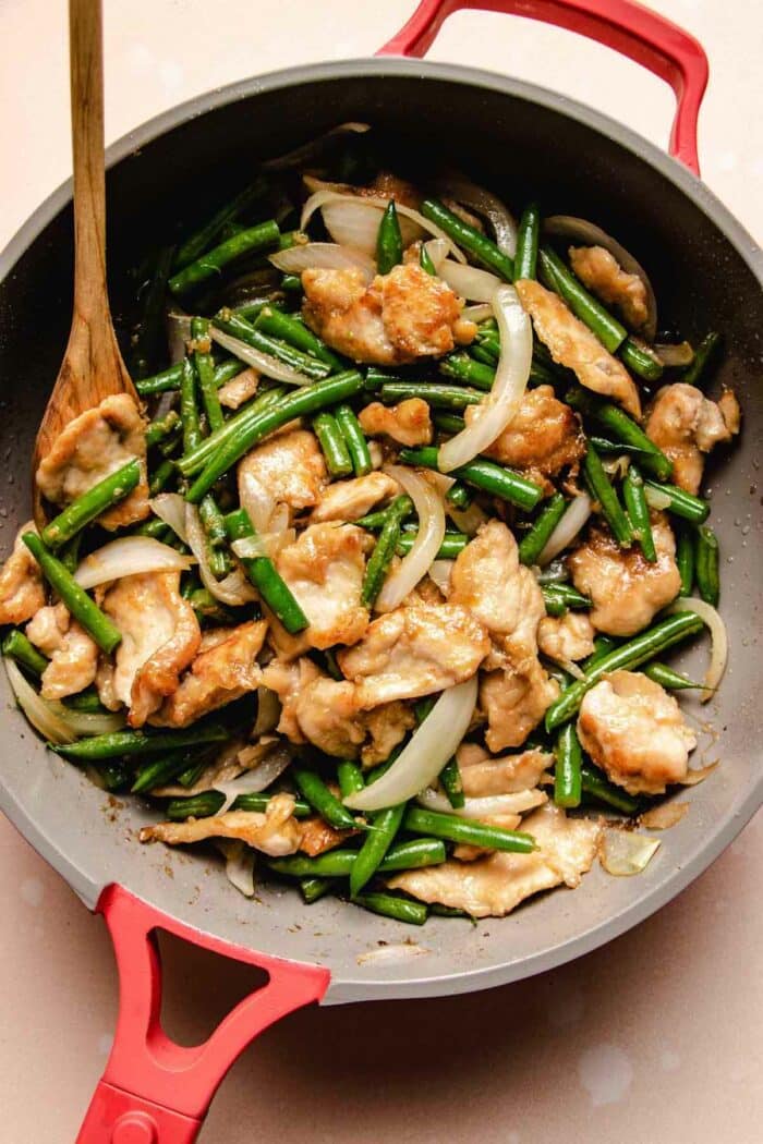 A close shot shows the stir fry chicken with green beans in a red color stir fry pan