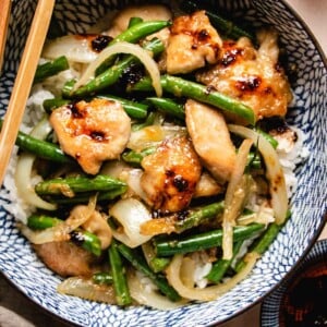 A close shot shows seared chicken breasts sauteed with green beans and onion served with white rice in a blue color bowl