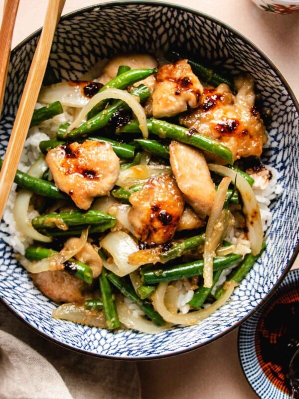 A close shot shows seared chicken breasts sauteed with green beans and onion served with white rice in a blue color bowl