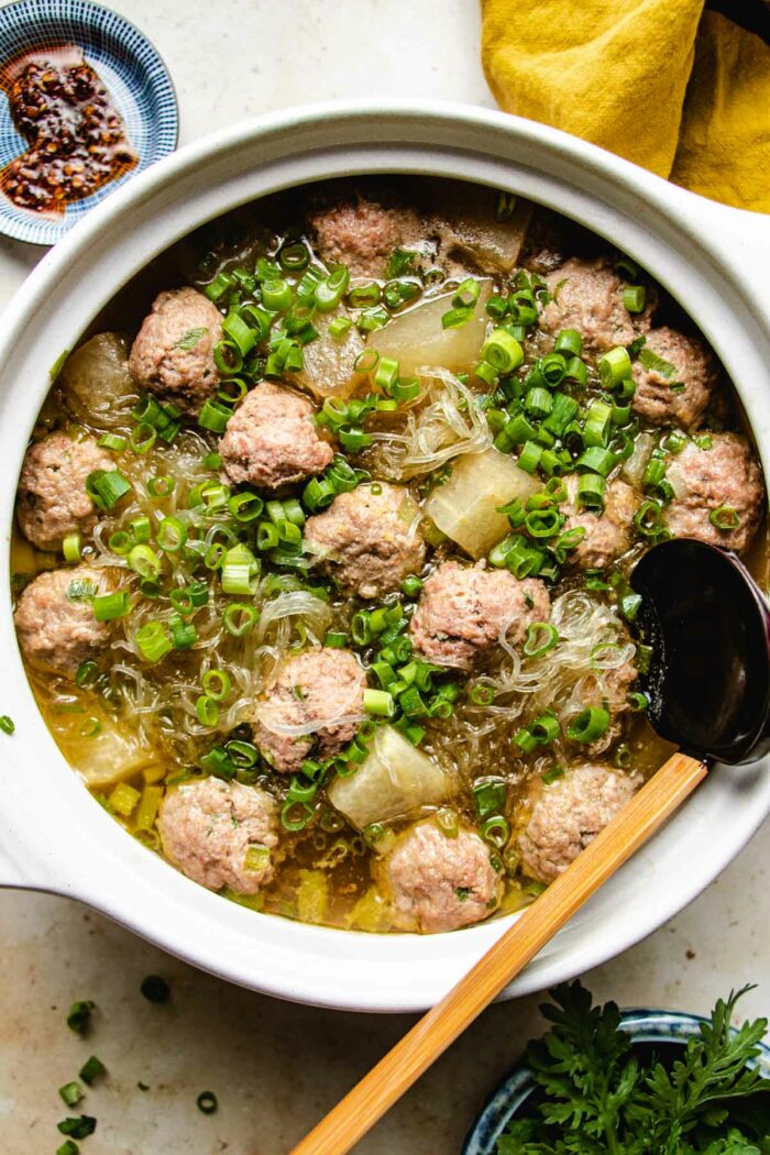 Winter melon and meatballs simmered in a big white clay soup pot with a ladle and extra sauce on the side