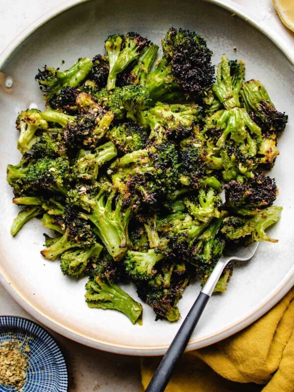 A close overhead shot shows crispy broccoli florets air fried from frozen and served in a white plate with a fork and yellow napkin on the side