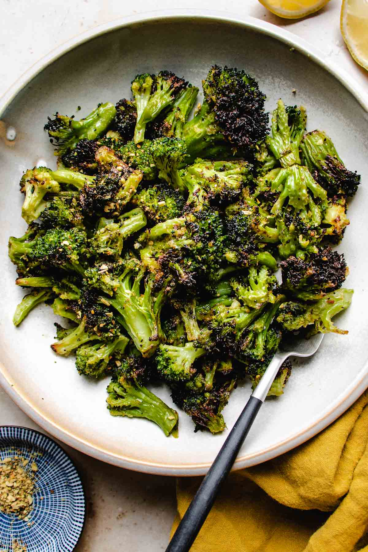 A close overhead shot shows crispy broccoli florets air fried from frozen and served in a white plate with a fork and yellow napkin on the side