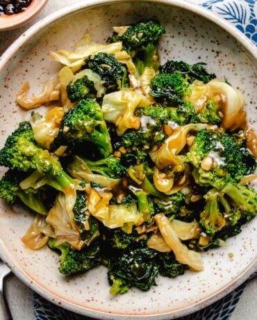 A close shot shows sauteed kale, broccoli, and cabbage served in a neutral color plate with blue napkins on the side.