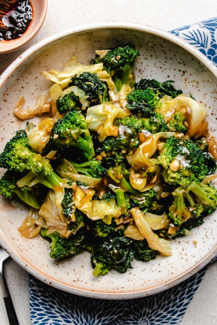 A close shot shows sauteed kale, broccoli, and cabbage served in a neutral color plate with blue napkins on the side.