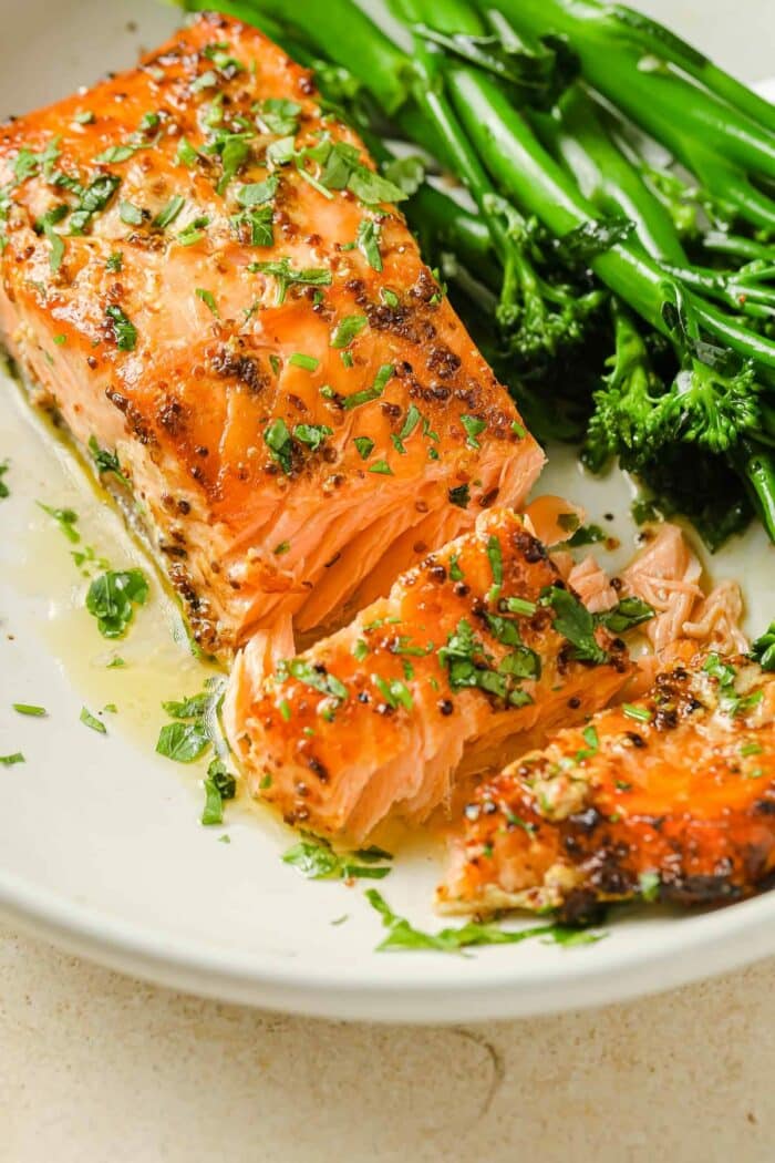 A close shot shows the moist and tender salmon fillets drizzled with dijon mustard sauce on a white plate