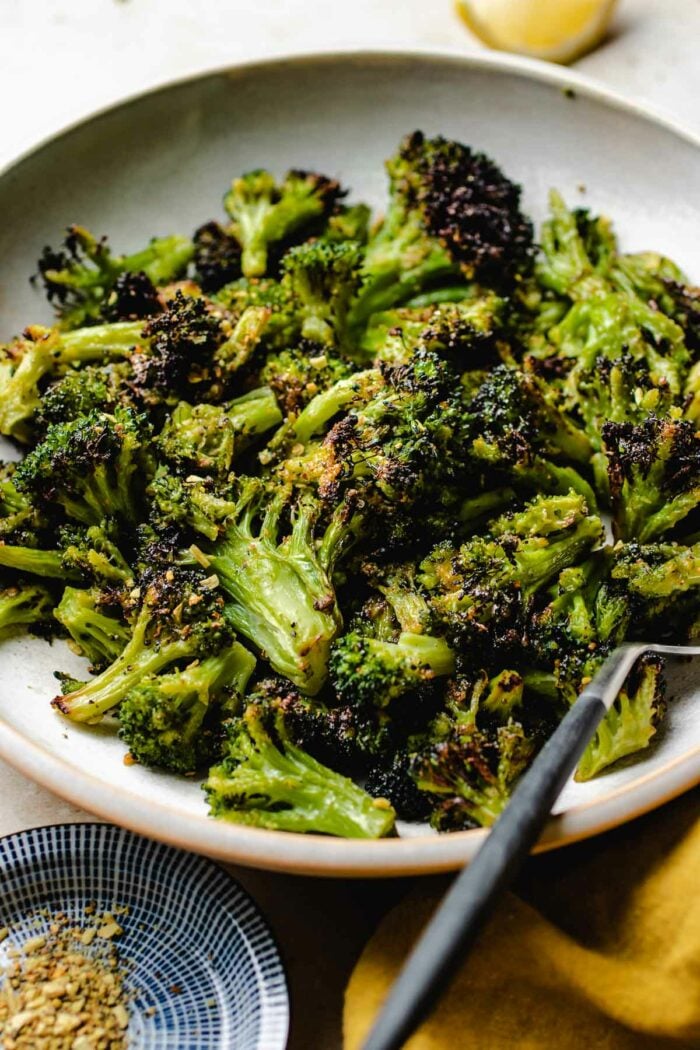 A side close shot shows crispy broccoli after air fried from frozen and with a fork on the side in a white plate