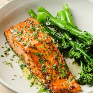 A close shot shows air fried salmon fillet with dijon mustard lemon sauce and broccolini on the side in a white plate