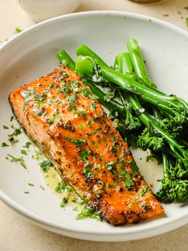 A close shot shows air fried salmon fillet with dijon mustard lemon sauce and broccolini on the side in a white plate