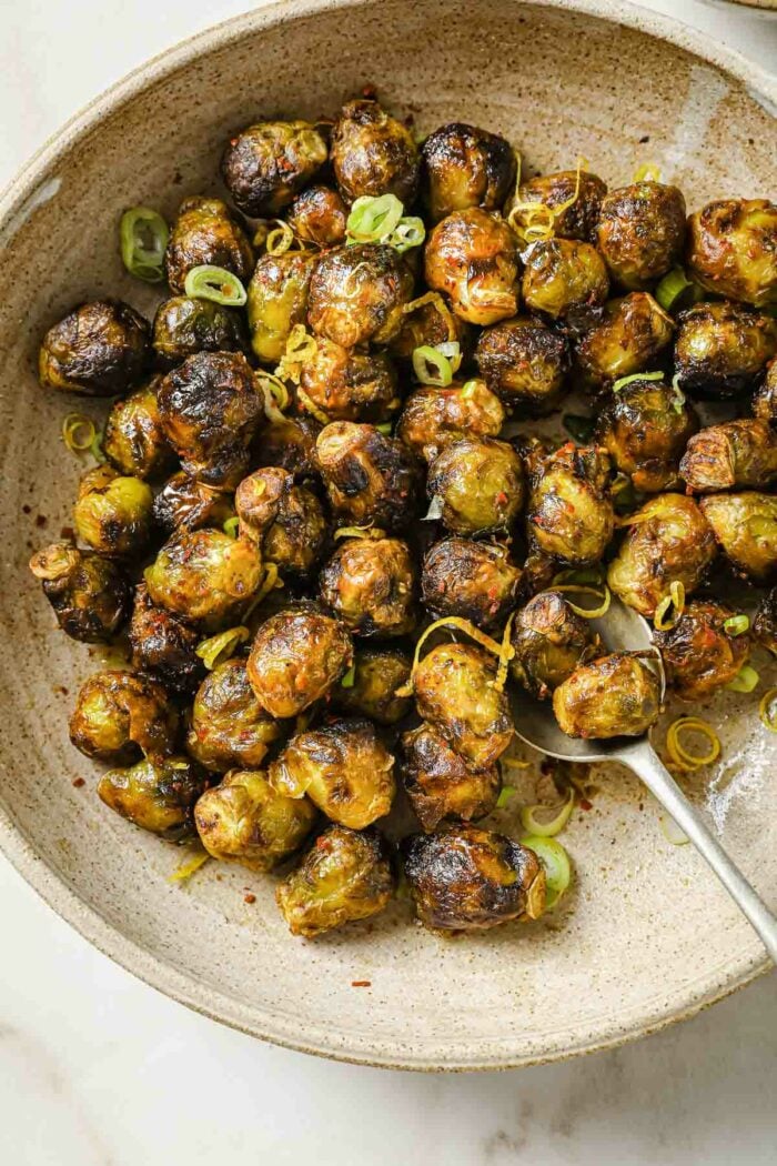 A close overhead image shows air fry frozen brussel sprouts with garnish on top and a serving spoon.