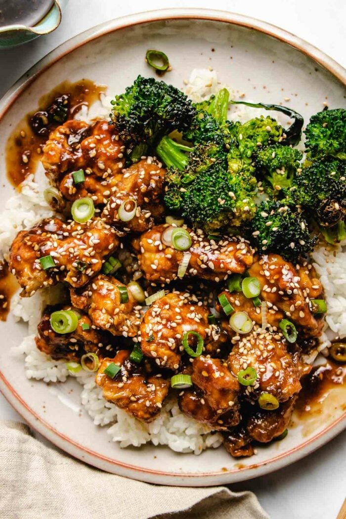 An overhead close photo shows air fried chicken chunks coated in teriyaki sauce, served with white rice and broccoli on the side.