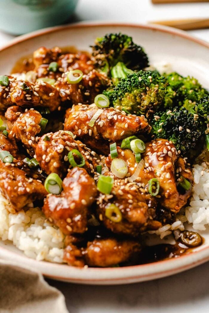 A side close shot shows air fried chicken coated in teriyaki sauce served with white rice and broccoli florets on the side.