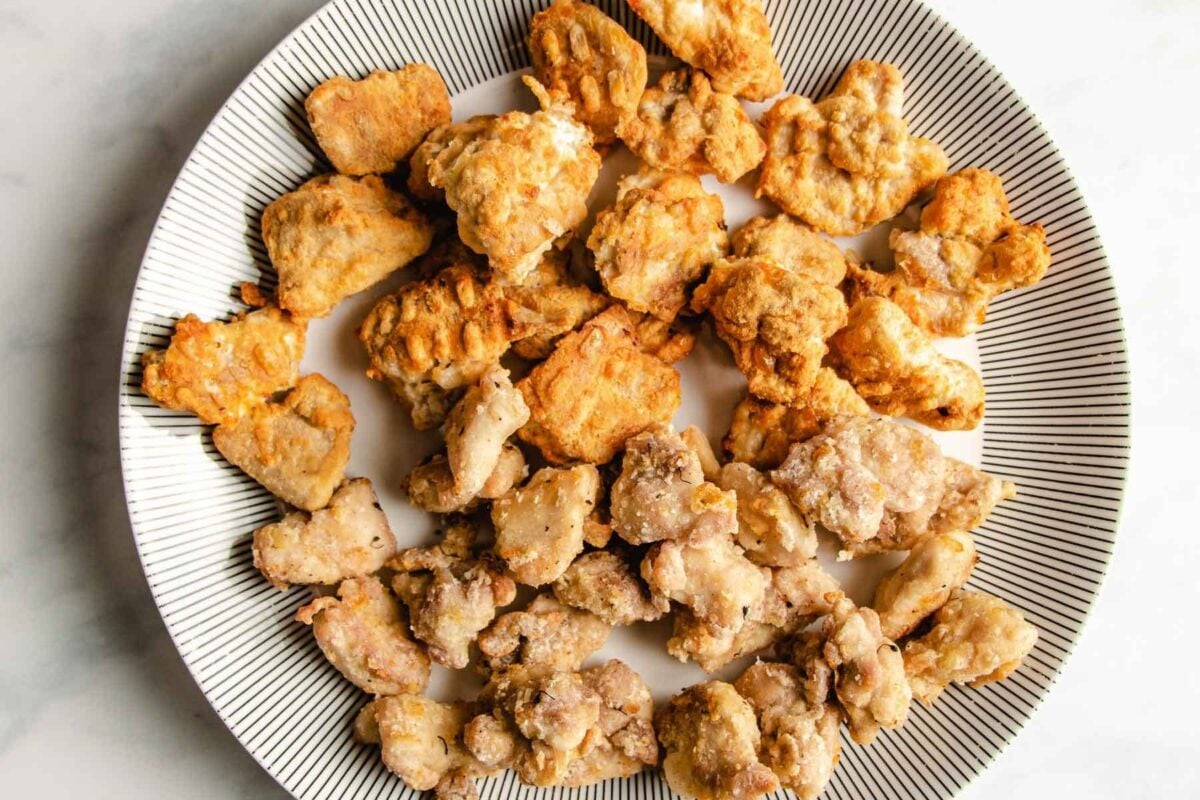 A plate with two types of air fried chicken pieces, including air fryer teriyaki chicken, one group golden and crisp, the other lighter and more lightly coated, all arranged on a white plate with a black striped pattern around the edge.