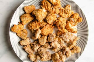 A plate with two types of air fried chicken pieces, including air fryer teriyaki chicken, one group golden and crisp, the other lighter and more lightly coated, all arranged on a white plate with a black striped pattern around the edge.