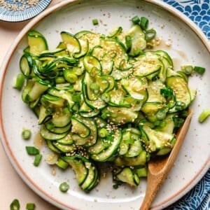 A feature image shows Korean zucchini slices chilled and served in a neutral color plate with a wooden spoon and blue color napkin on the side