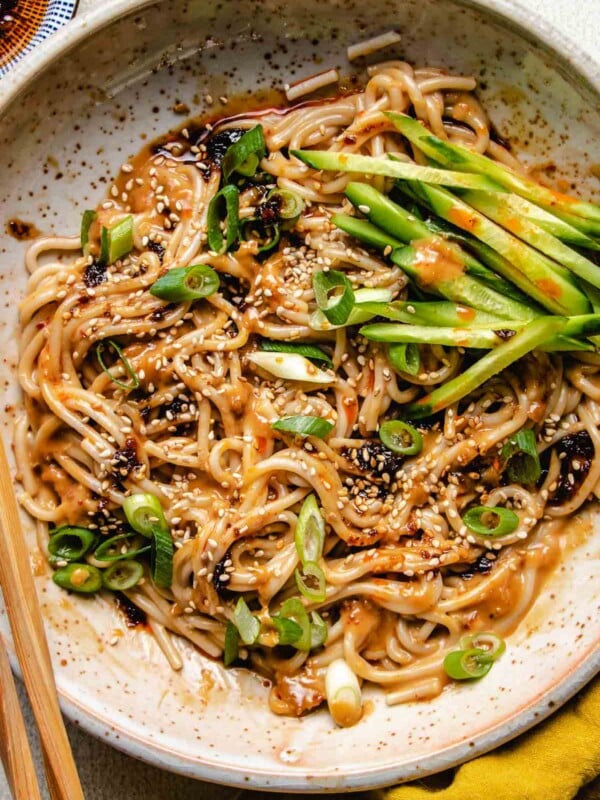 An overhead close shot shows the cooked noodles tossed with peanut sauce with diced cucumbers on the side in a neutral color plate.