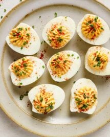 An overhead close shots shows air fried devilled eggs garnished with paprika and chive over a neutral color plate