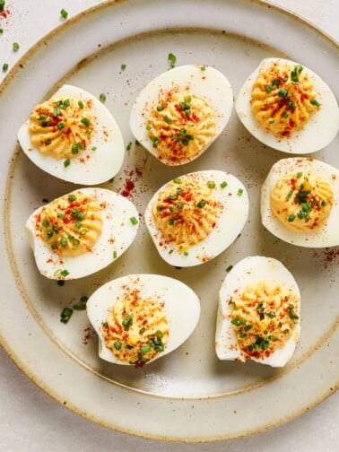 An overhead close shots shows air fried devilled eggs garnished with paprika and chive over a neutral color plate