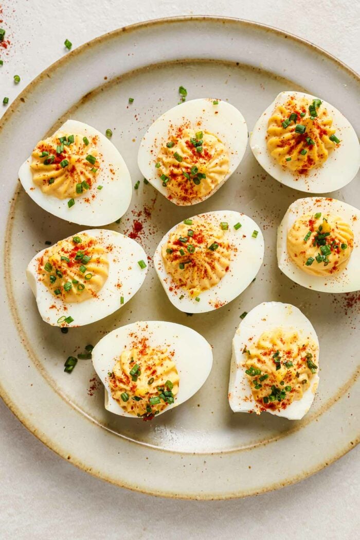 An overhead close shots shows air fried devilled eggs garnished with paprika and chive over a neutral color plate
