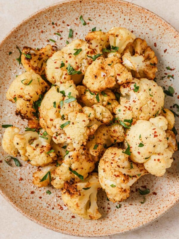 An overhead shot shows cauliflower florets air fried to golden crispy and served over a neutral color big plate