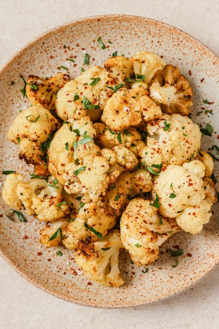 An overhead shot shows cauliflower florets air fried to golden crispy and served over a neutral color big plate
